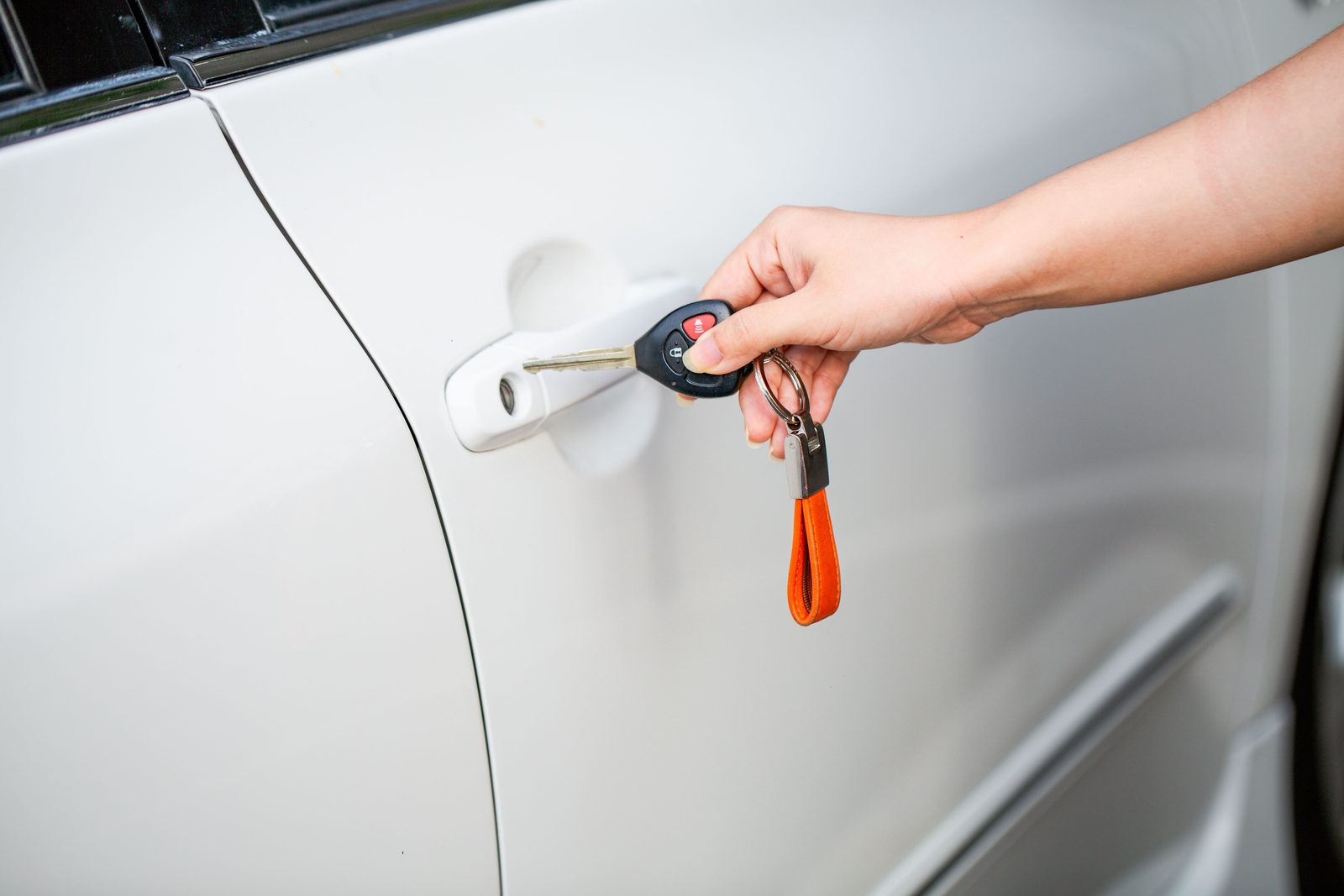 A hand holding a transponder car key with a small remote at a car door